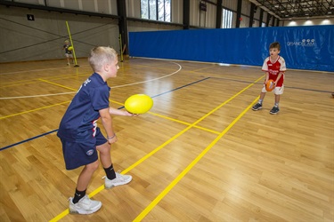 Two children practise handballing and AFL ball