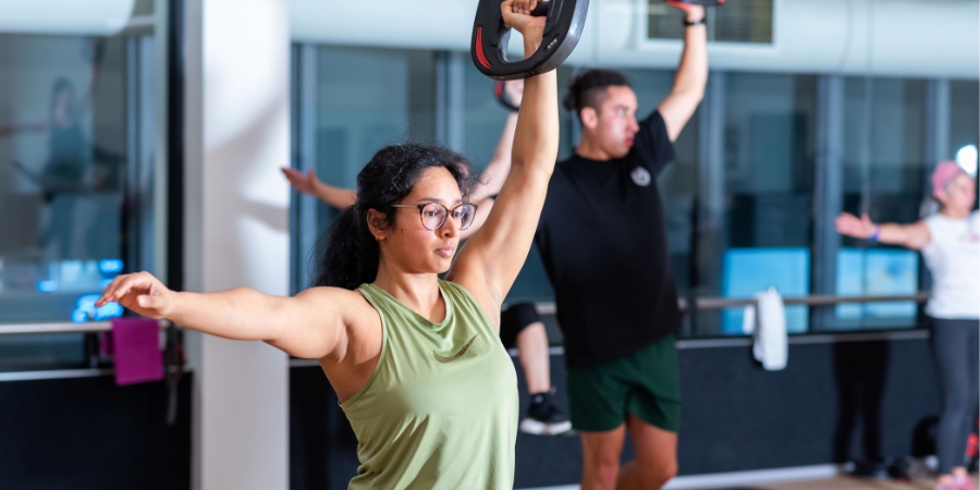 Close up of people lifting barbells with one arm in an indoor group fitness class