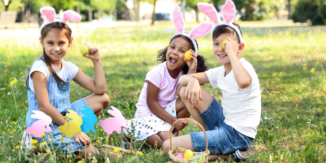 Three children wearing bunny ears and holding plastic eggs