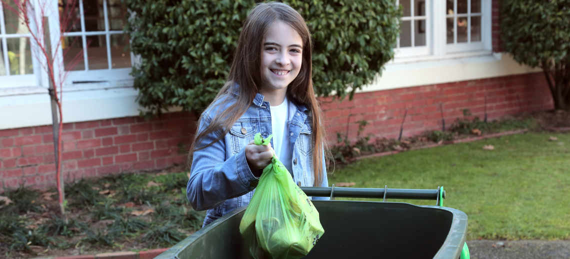 Young person putting a green liner filled with organic waste into their FOGO bin.
