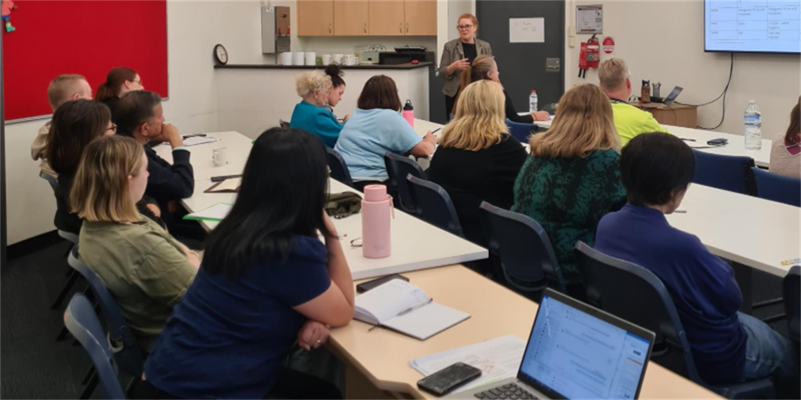 People sitting at desks listening to a workshop presenter