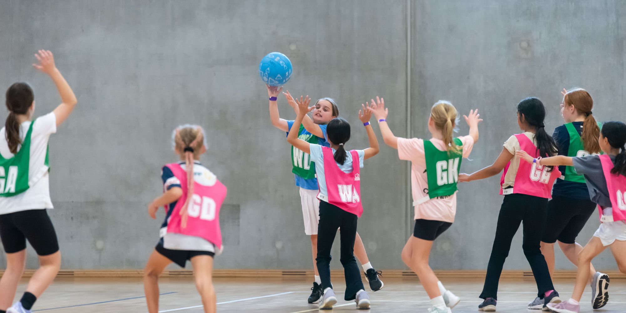 Children playing a netball game indoors on a sports court.