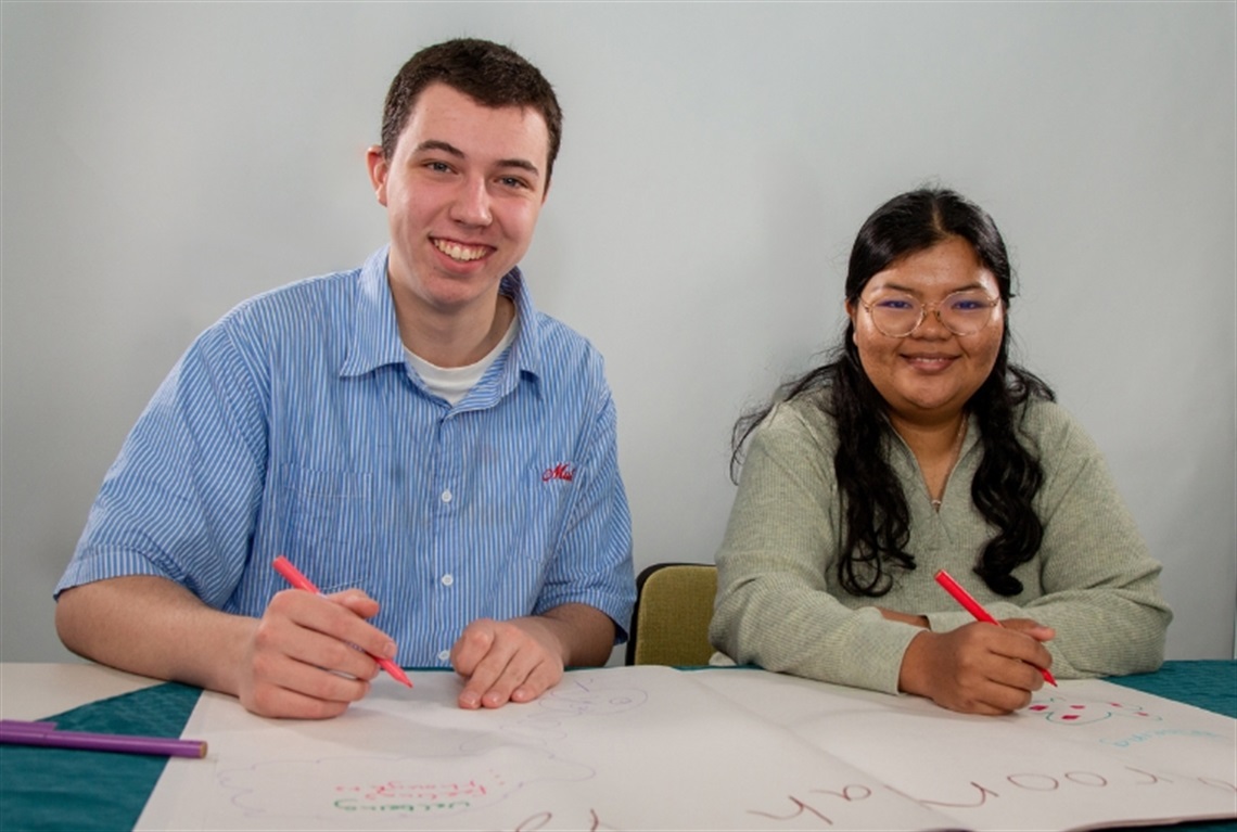 Two young people sitting at a table writing on butchers paper