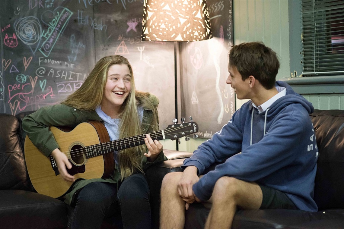 Teenage girl sitting on a couch smiling playing the guitar at EV's Youth Centre .jpg