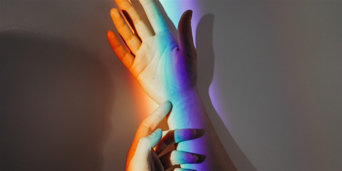 Two hands with a rainbow reflection shining across them