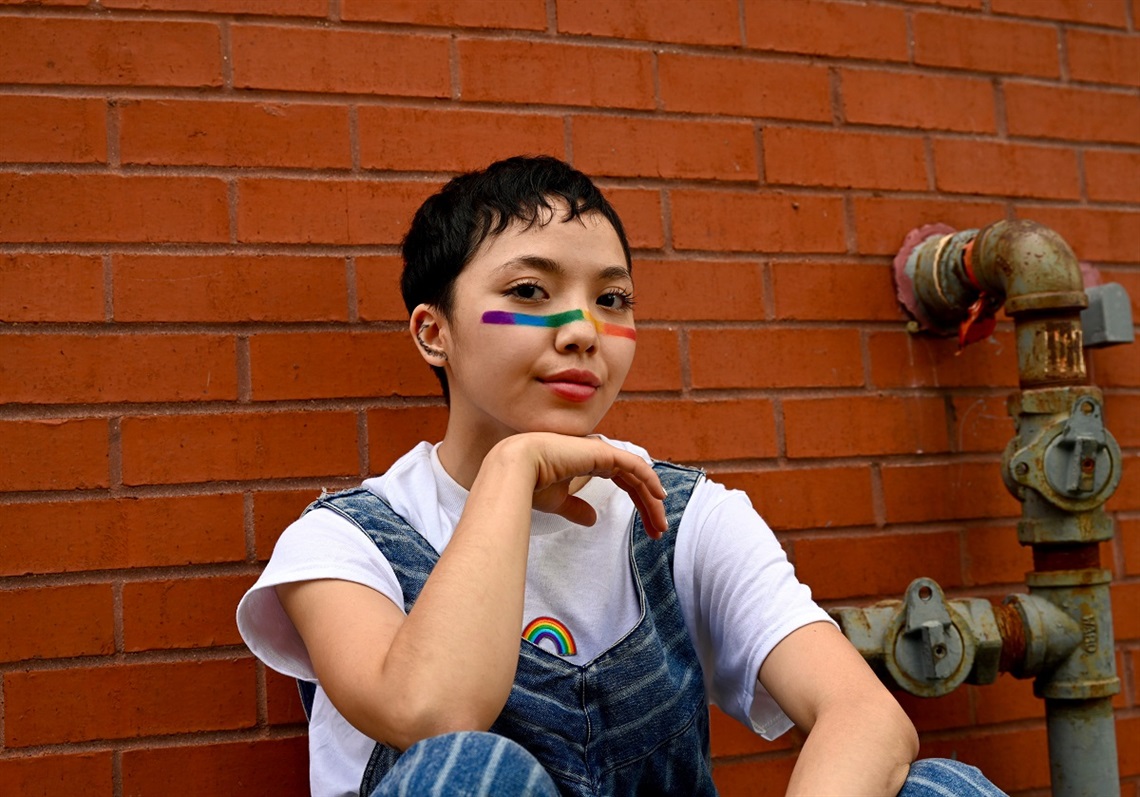 Woman with rainbow painted on her cheeks sitting in front of a brick wall.jpg