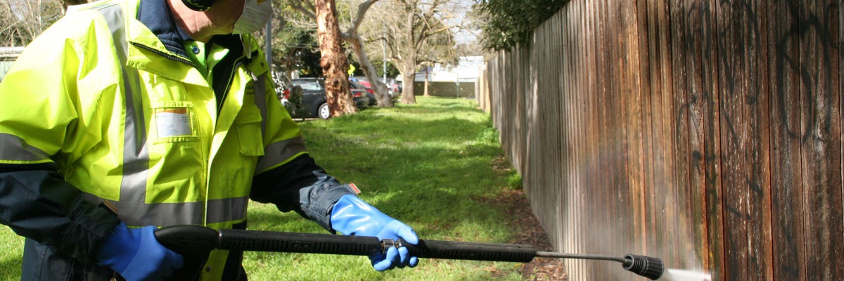 Council staff member using a paint gun to paint over graffiti on a fence
