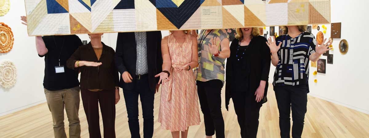 7 members of the Arts & Culture team standing in an exhibition space and holding an artwork up over their faces