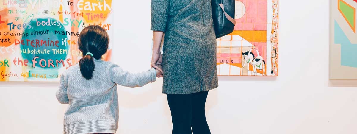 an adult and a child holding hands, looking up at artwork in an exhibition