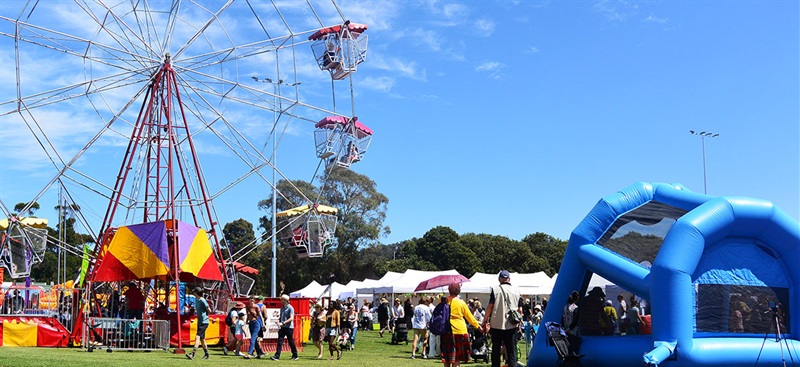 Image of ferris wheel, surrounded by white marquees and lots of people milling around