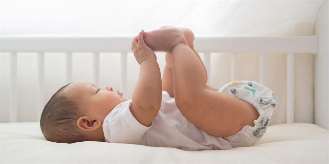 baby holding toes in cot