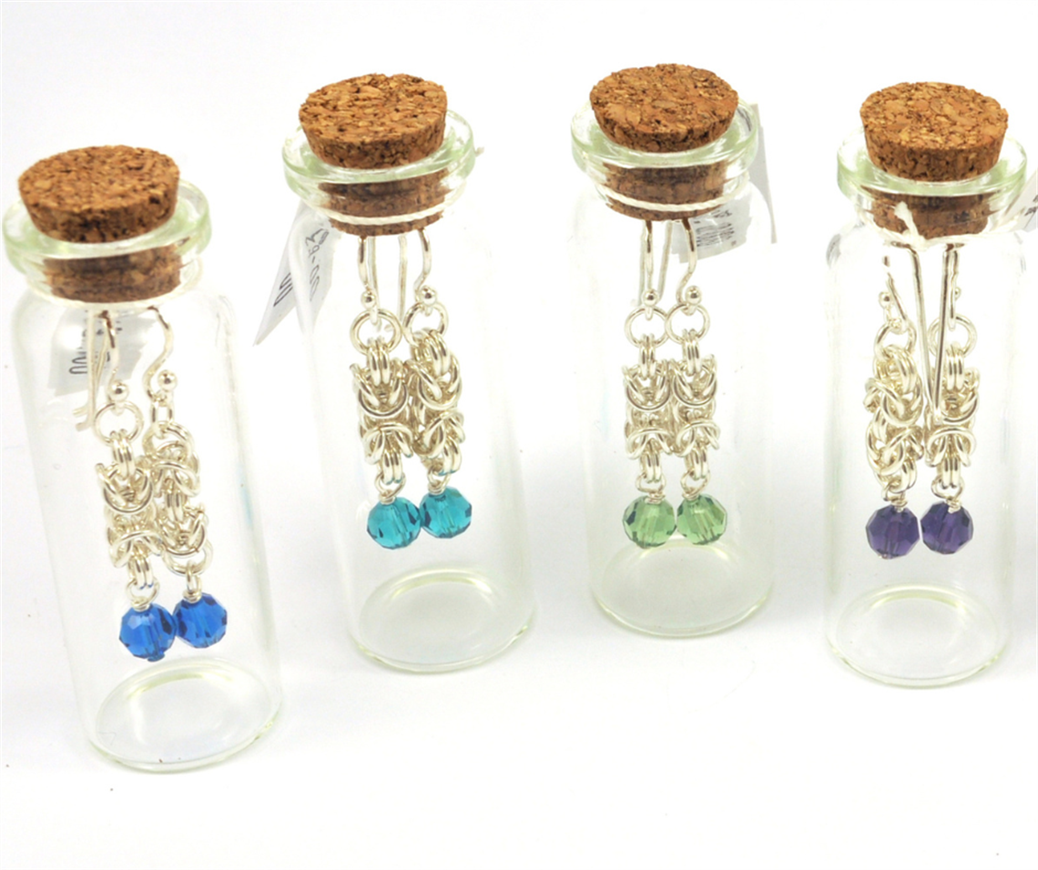 4 glass jars with corks in the top. Silver earrings with crystal beads are inside the jars, hanging from the cork.