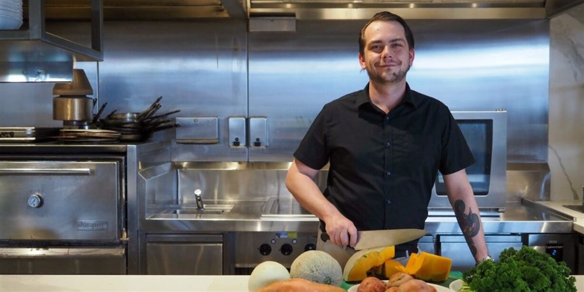 Chef Nathan standing in an industrial kitchen with fresh produce in front of him.