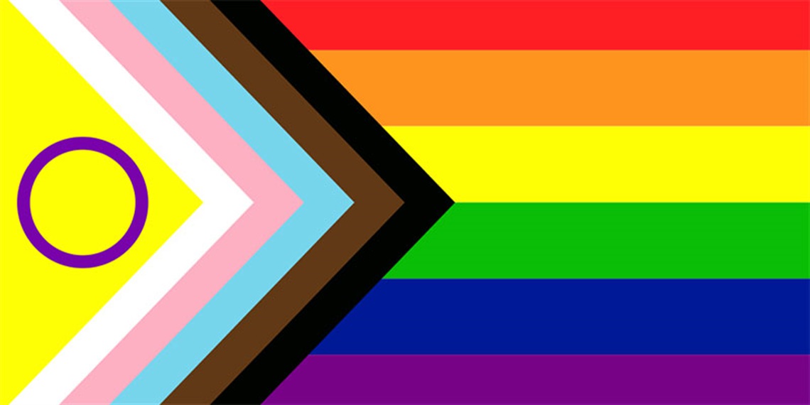 inclusive pride flag including rainbow colours in horizontal stripes across the flag. There is a triangle of colours on the left hand side of the flag which includes black and brown to represent people of colour; pink, light blue and white to represent trans, gender non-binary, intersex and those across the gender spectrum; and a purple circle in a yellow triangle which represents intersex people.