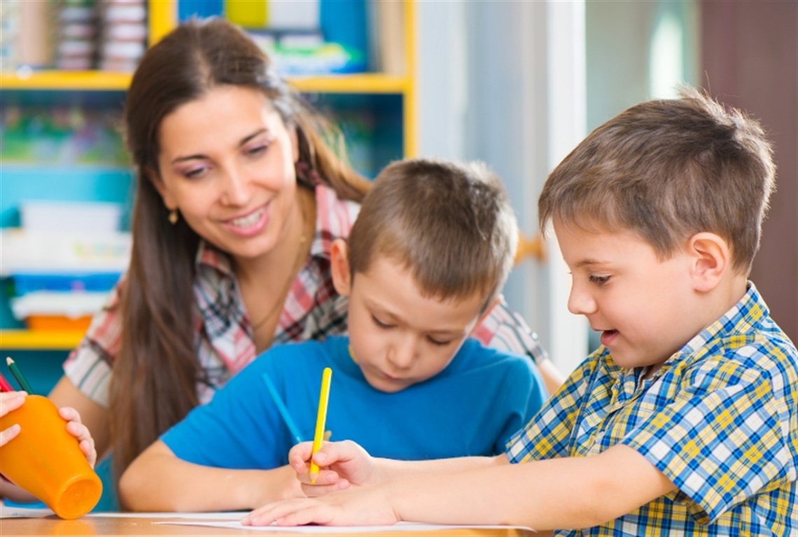 an educator sitting at a table with two children who are using pencils