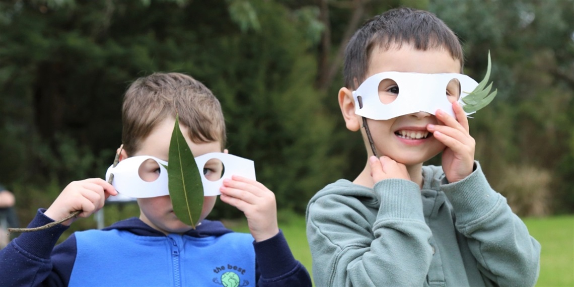 Two young children holding masks to their face, made from paper and leaves
