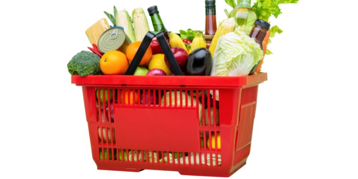 Red shopping basket filled with fresh produce, canned goods, and glass bottles.