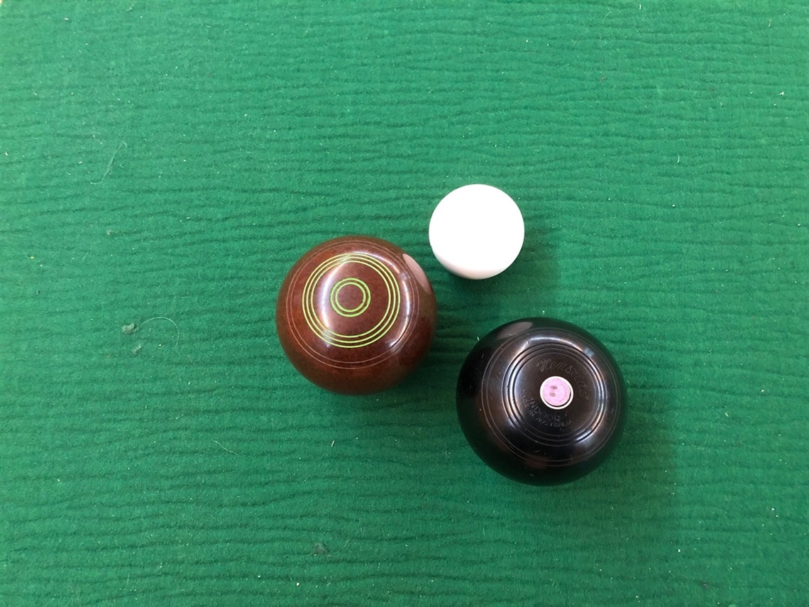 A large brown ball and a large black ball sitting close to a small white ball on a green background