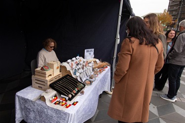 Visitor viewing handmade jewellery and accessories at a market stall.