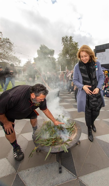 People standing near a smoking ceremony with eucalyptus leaves and rising smoke.