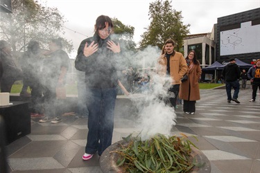 Smoking ceremony with eucalyptus leaves burning as people gather in an outdoor public space.