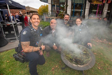 Community members gathered around a smoking ceremony outdoors with smoke rising from a fire bowl.