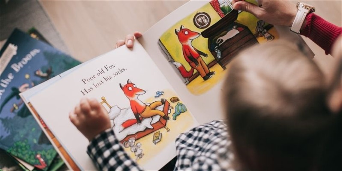 A child sitting with an adult as they read a picture book about a fox.
