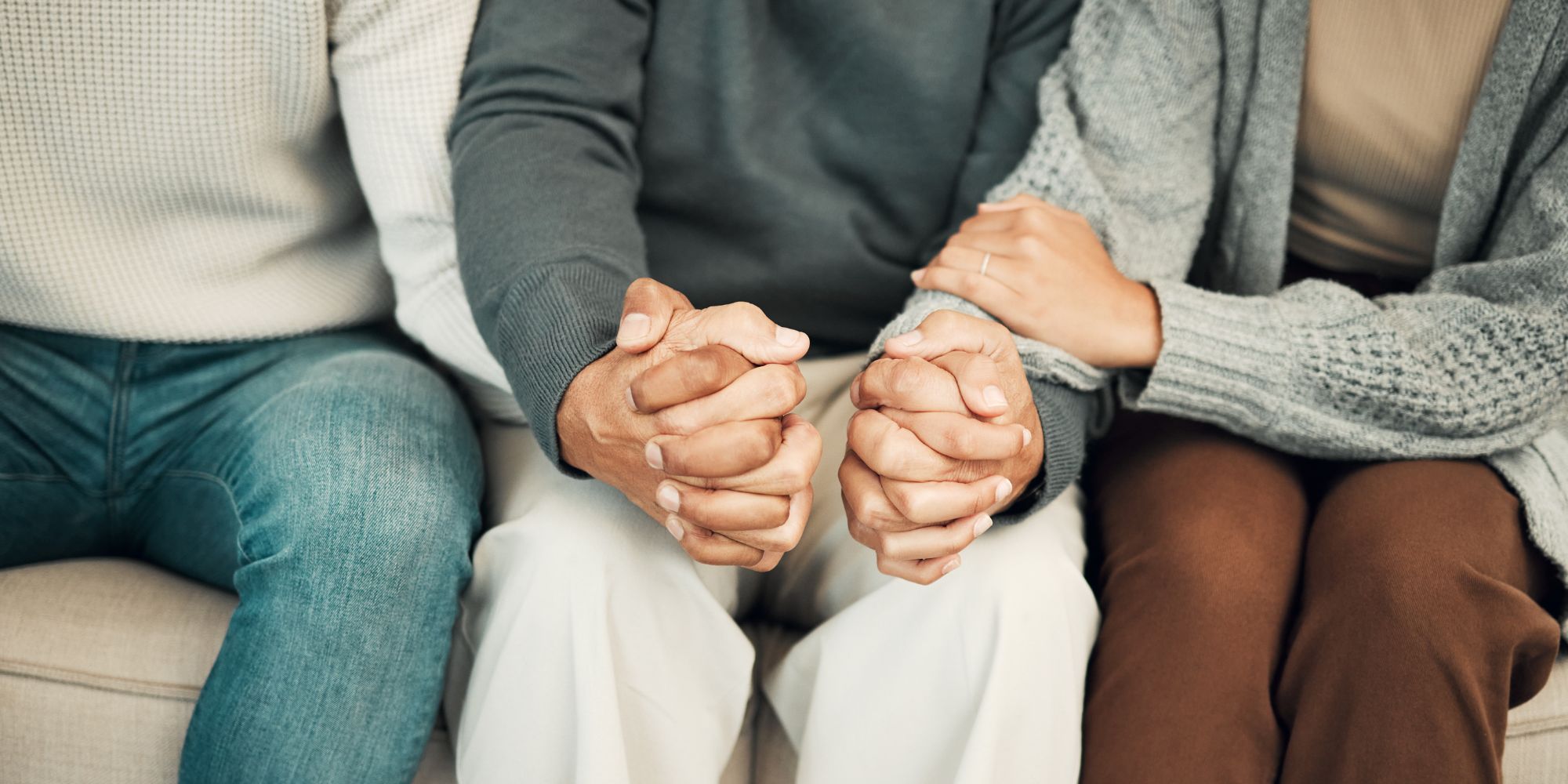 Three people sitting on a couch with hands clasped, one person holding another's arm.
