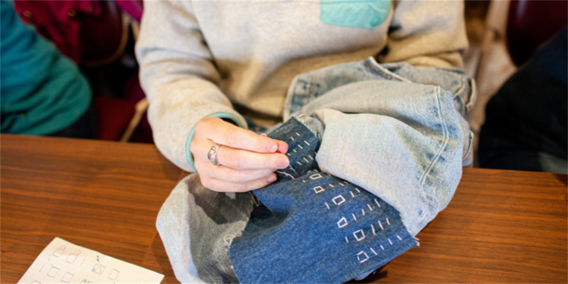 Someone hands stitching and mending denim jeans.png
