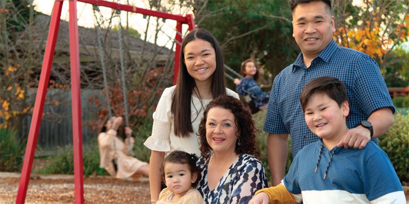 family standing in playgorund while children play on swings behind them