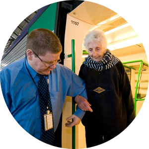 A Metro Trains employee helping an older person step off a train. They are standing at the train door on a platform.