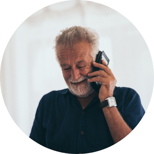 An older person holding a mobile phone to their ear. They are indoors and appear to be having a phone call.