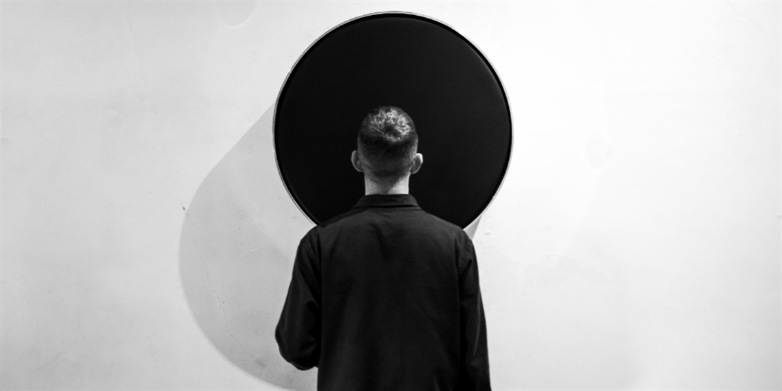 A black and white photo of a person standing in front of a black drum on a wall