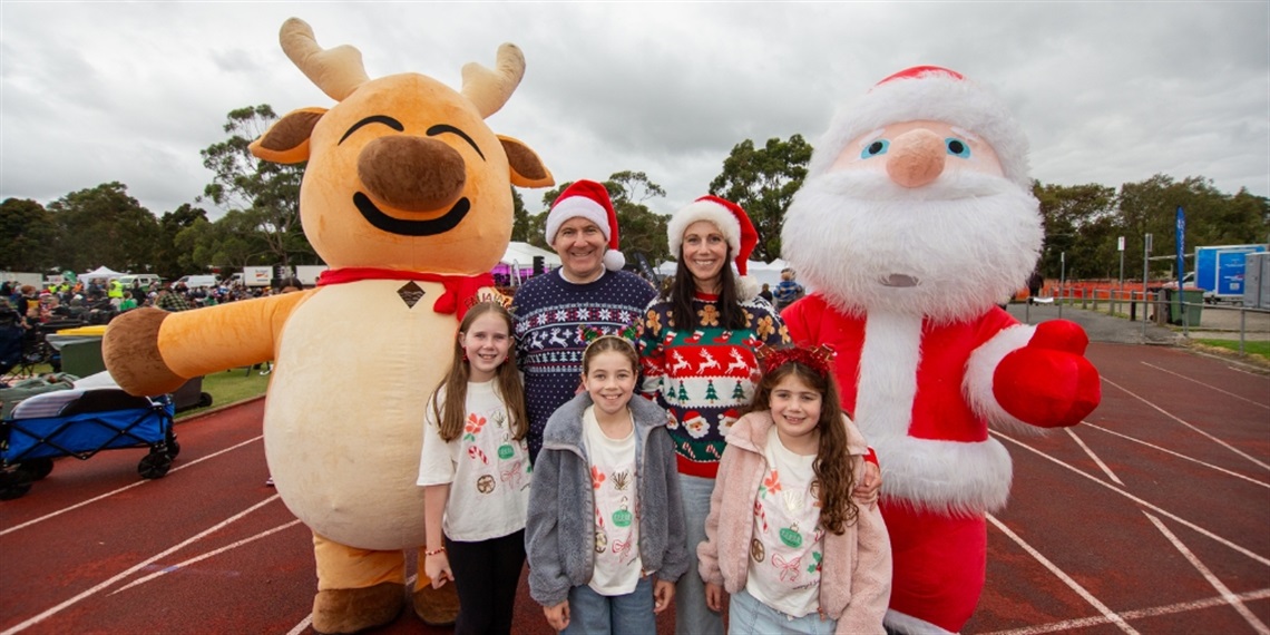 A family in Christmas outfits, standing with a large reindeer and Santa