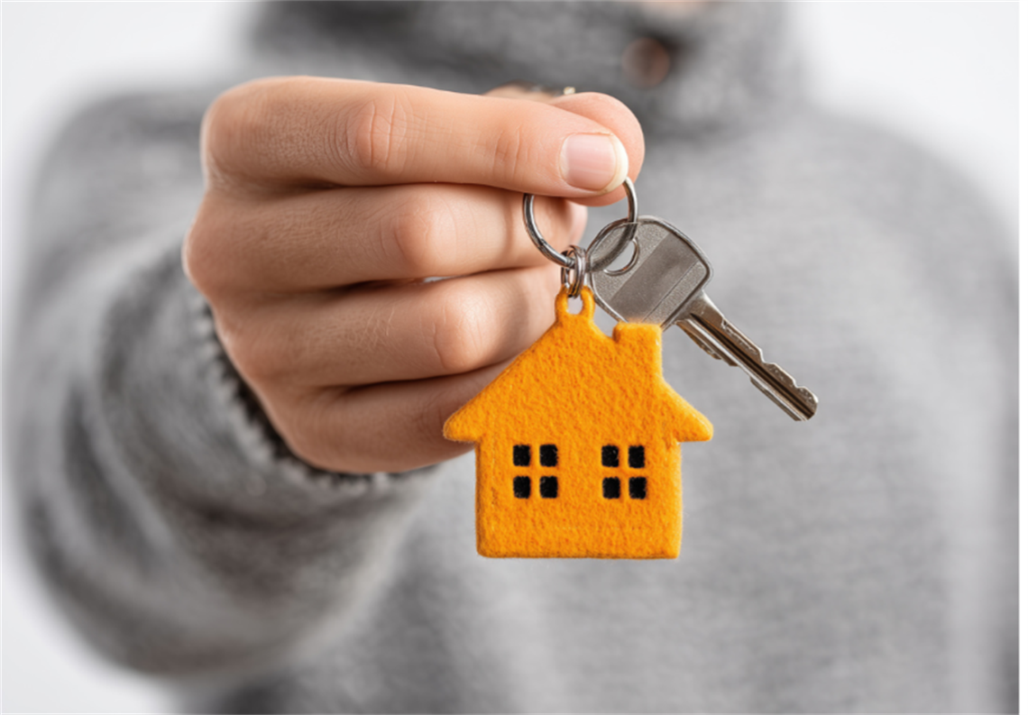A hand holds a key with an orange house-shaped keyring.