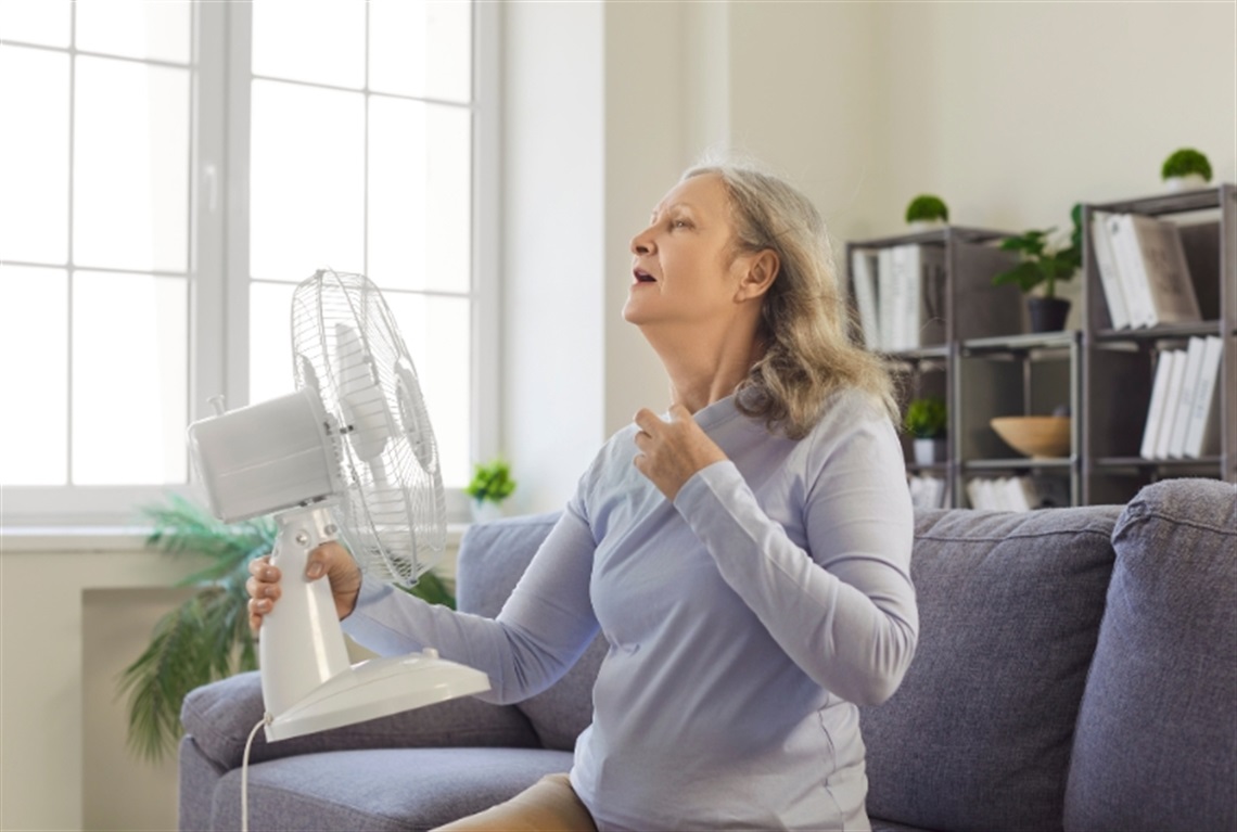 A woman is sitting on a counch and holding a fan in front of her